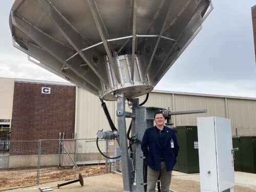 Michael Cratt standing in front of a satellite dish next to a building